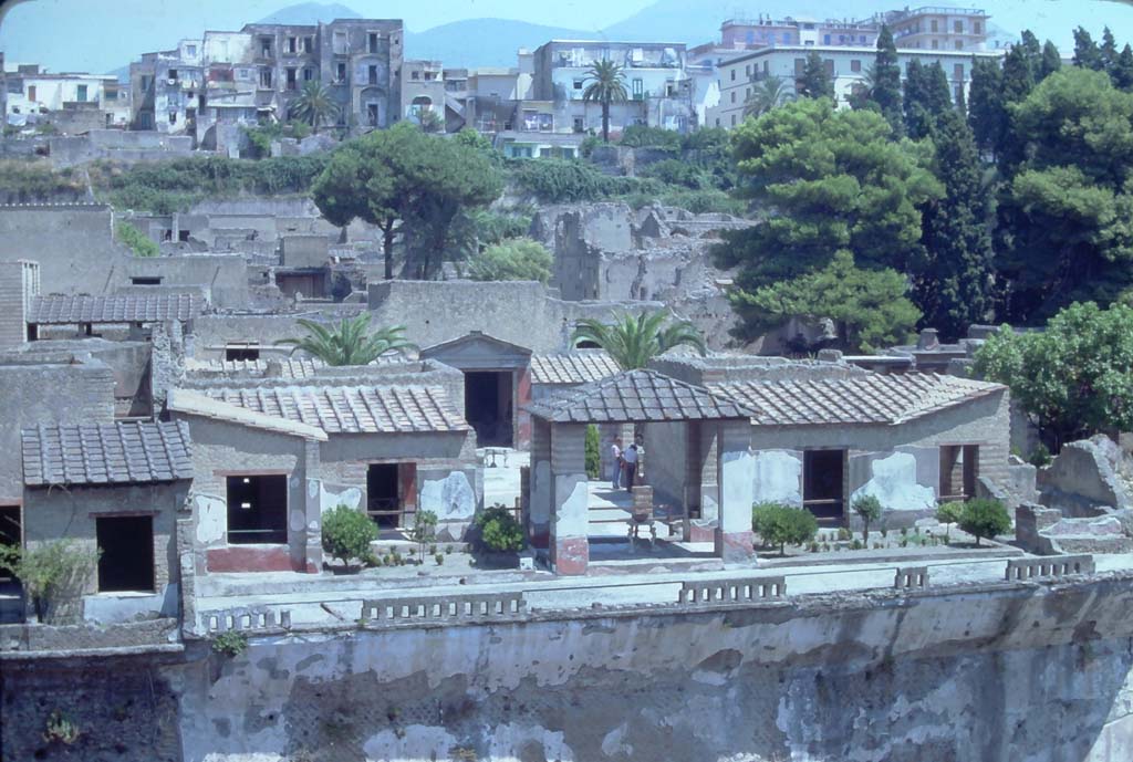 IV.21, Herculaneum. 7th August 1976. Looking north across terrace 35, towards pergola 18, (in centre) from access roadway to site.
On either side of the pergola was a small rectangular garden.
Rooms 23 and 22, daytime cubicula, can be seen on either side of the gardens, (on left, and on right side, without a roof).
Photo courtesy of Rick Bauer, from Dr George Fay’s slides collection.
